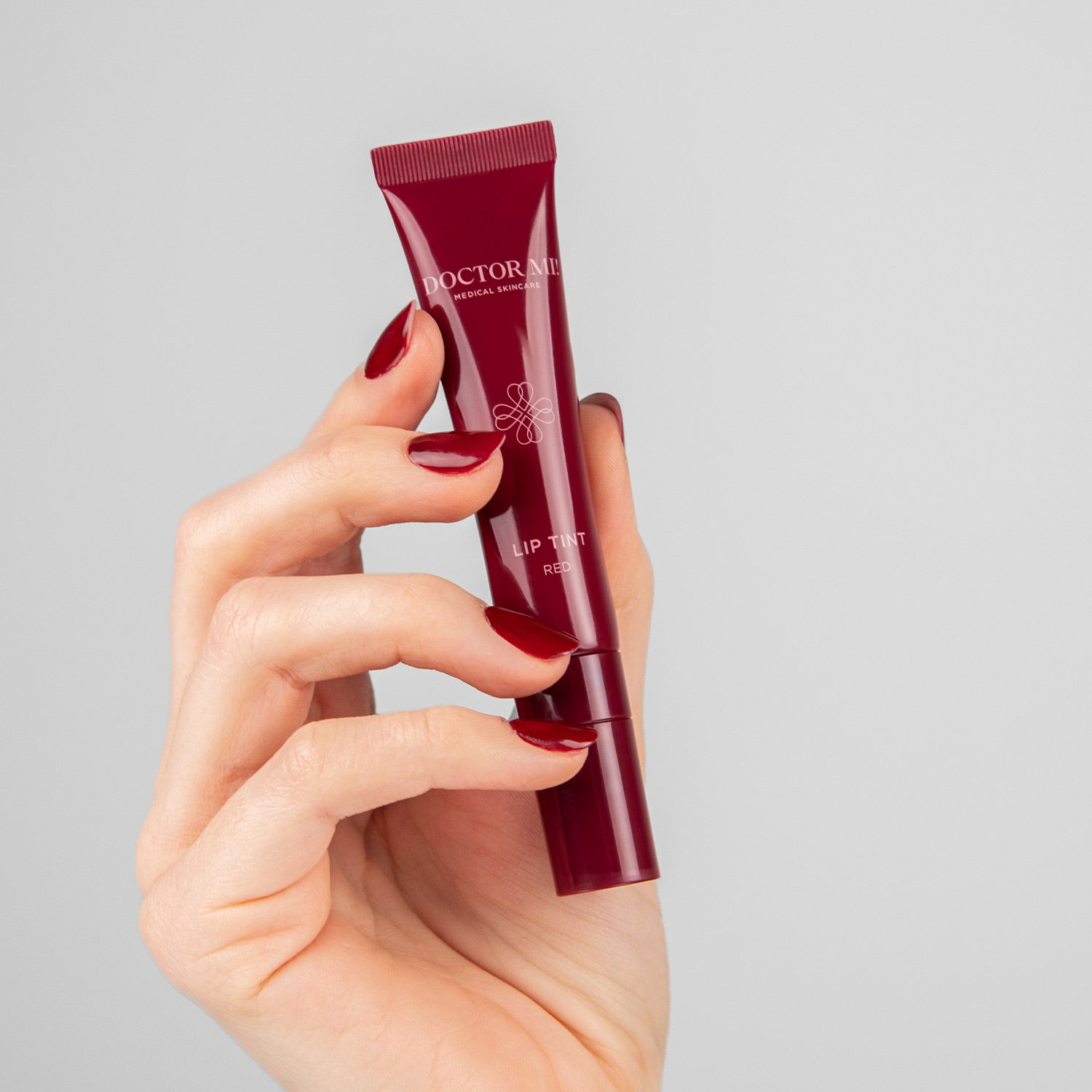 DOCTOR MI! PLUMPING LIP TINT innovative Lippenpflege mit einem Hauch von Farbe für eine gestärkte Hautbarriere in roter Tube in Hand auf grauem Hintergrund 
